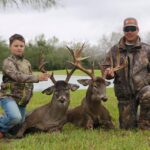 Father and son hunters kneel beside their trophy whitetail bucks.