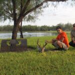 Young men after the hunt kneeling beside their whitetail buck by an El Monte Gringo Ranch sign