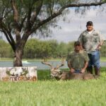 Two men next to their large whitetail buck and the El Monte Gringo Ranch sign