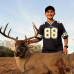 A young boy kneeling beside a large whitetail buck deer,