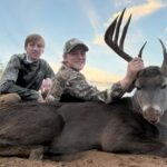 Young men pose with their large whitetail buck kill