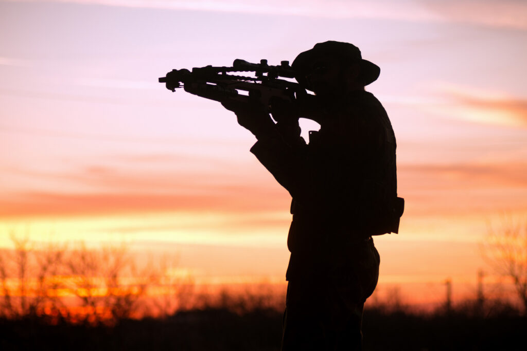 Crossbow hunter aiming at a whitetail deer hunt in Texas silhouetted against the sunset